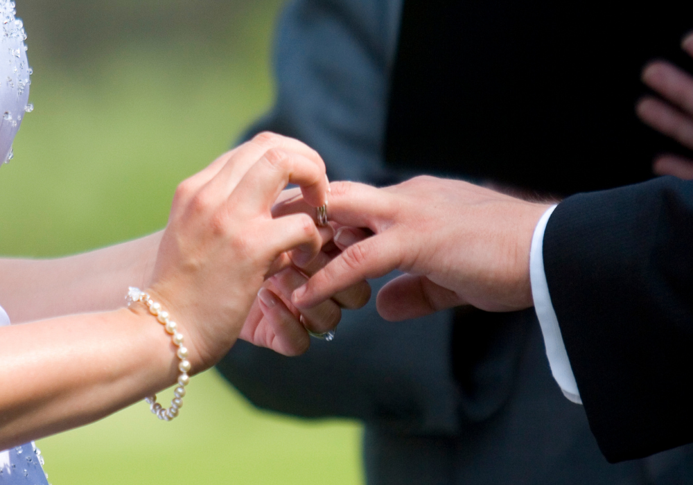 Close up of a bride and grooms hands during an elopement. The bride slides the grooms ring on his wedding finger.